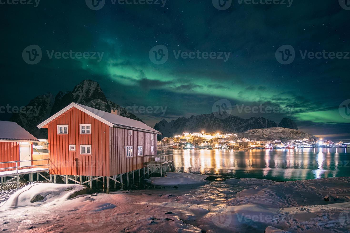 Red wooden house in fishing village with aurora borealis over Reine town in winter at night photo