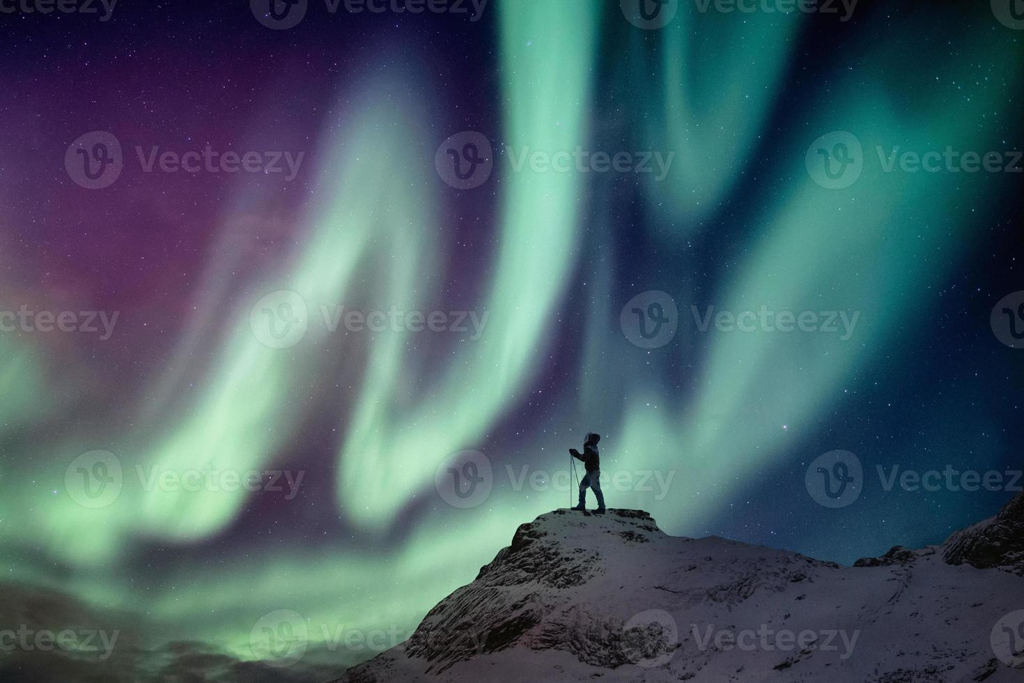 Man climber standing on snowy peak with aurora borealis and starry photo