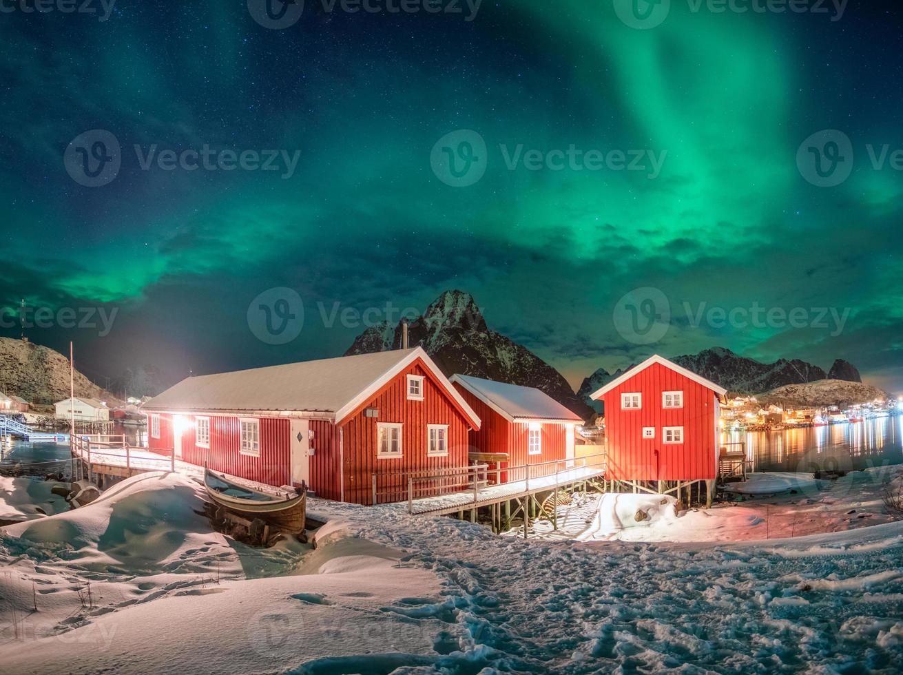 Casa roja en pueblo de pescadores con aurora boreal sobre el océano Ártico en invierno por la noche foto