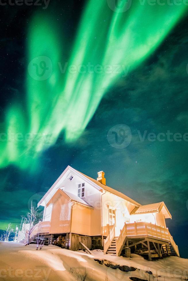 Aurora Borealis Northern Lights sobre la casa blanca iluminada con nieve en invierno foto