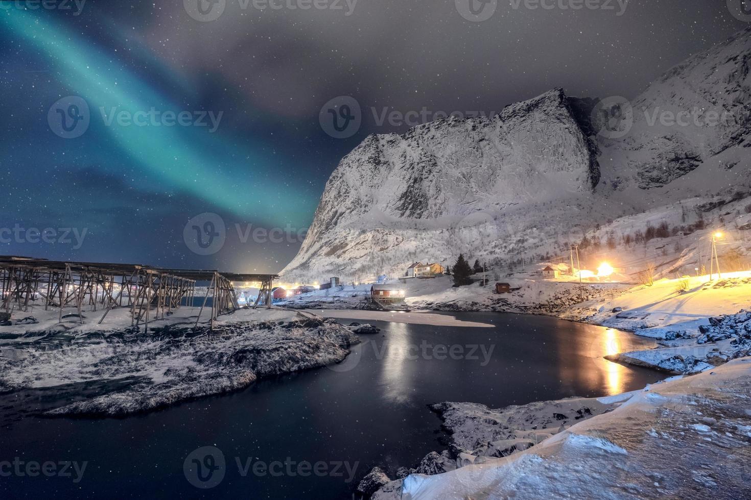 Iluminación de la aldea escandinava con luces del norte brillando en la montaña nevada foto