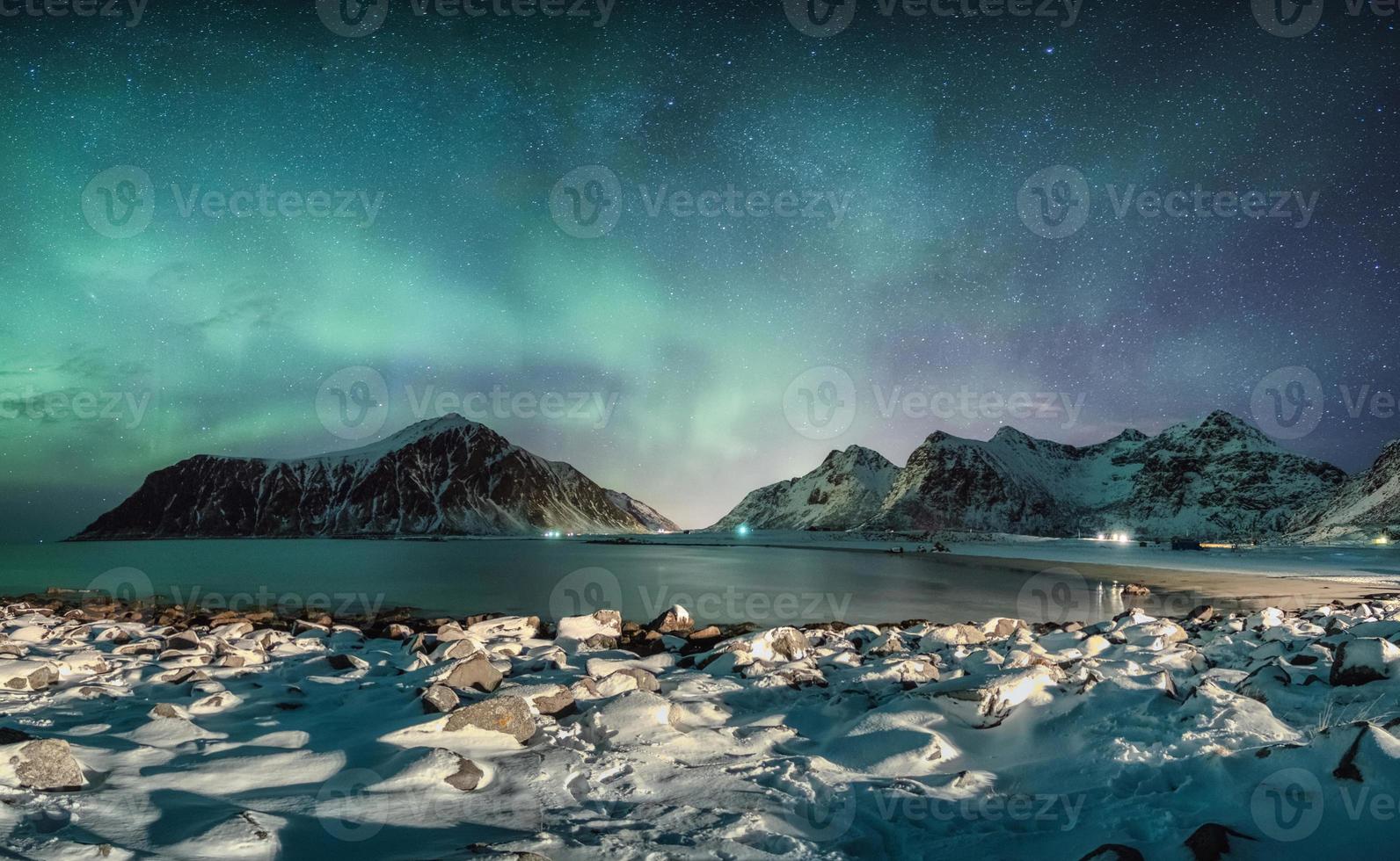 Aurora borealis with stars over mountain range with snowy coastline at Skagsanden beach photo