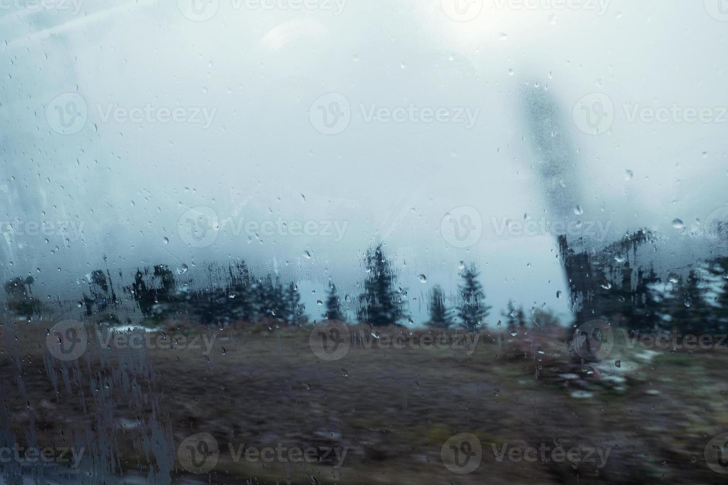 Gota de vapor de agua en la ventana transparente de camino al bosque foto