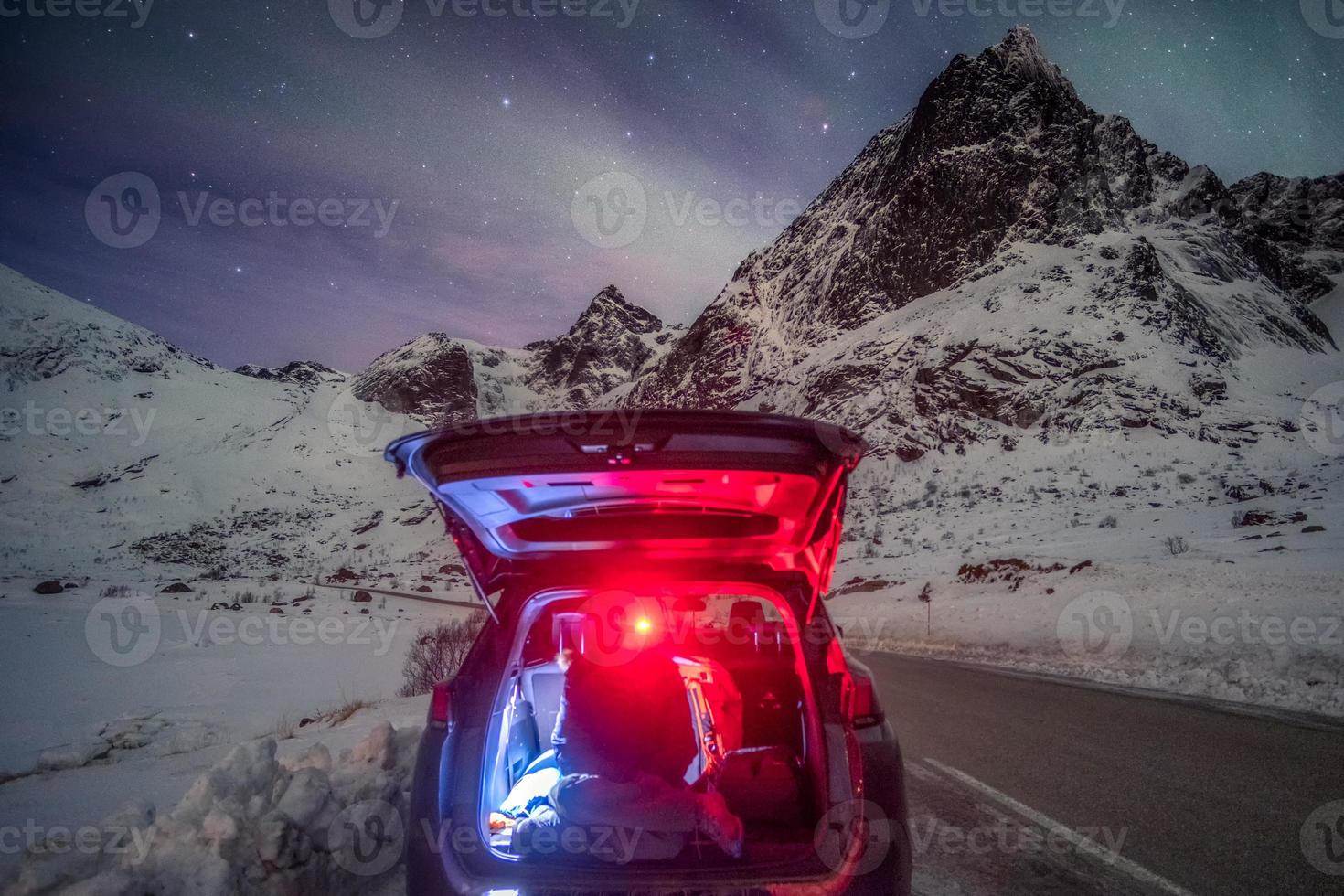 Turista hombre sentado en la parte trasera del coche en la montaña rodeada de auroras boreales foto