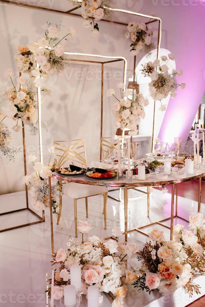 el presidium de los recién casados en el salón de banquetes del restaurante está decorado con velas y plantas verdes, el tono general del salón es beige foto