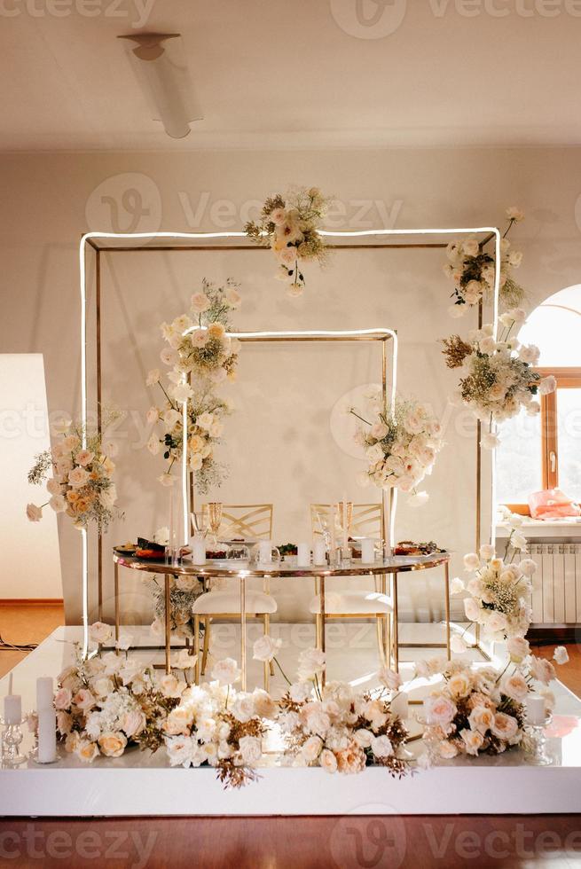 the presidium of the newlyweds in the banquet hall of the restaurant is decorated with candles and green plants, the general tone of the hall is beige photo