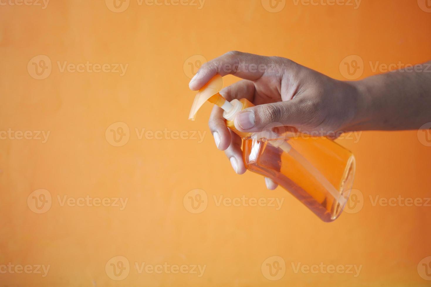 Sosteniendo el líquido de lavado de manos en un recipiente sobre fondo naranja foto