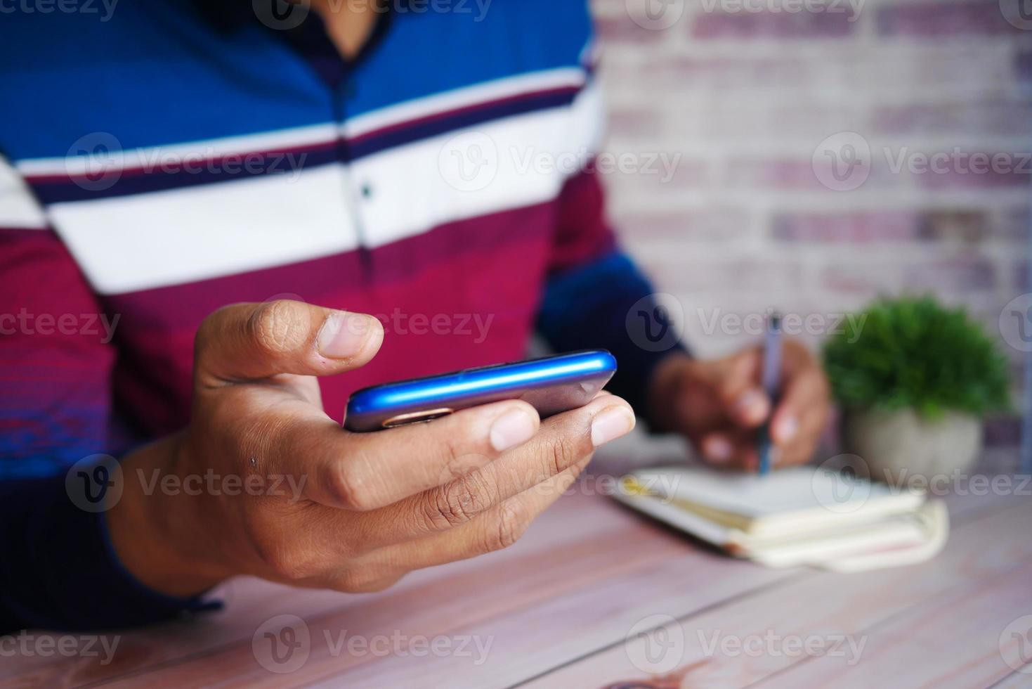 Young man hand holding smart phone and writing on notepad while sited photo