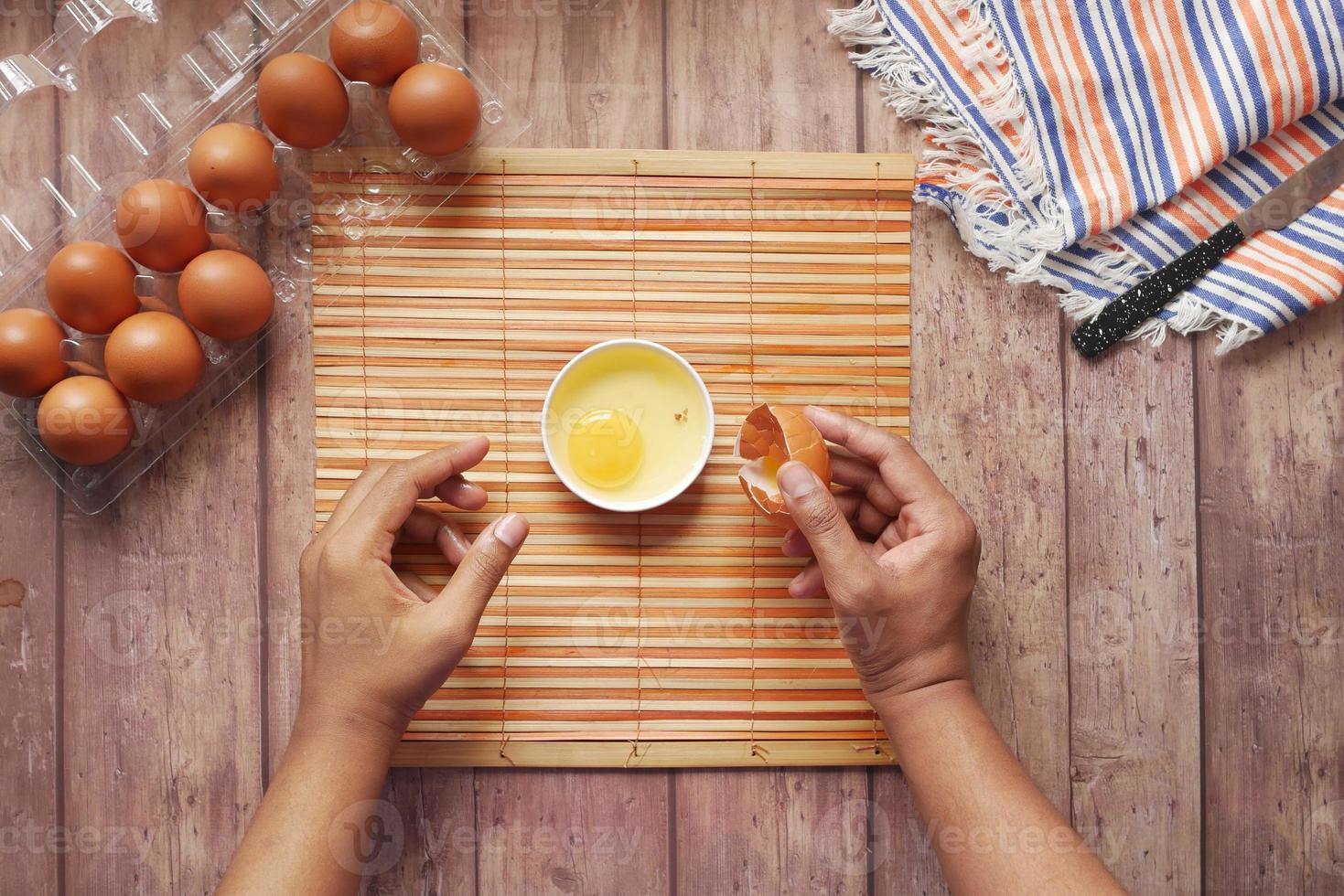 Man breaking egg and pouring into a small container on table photo