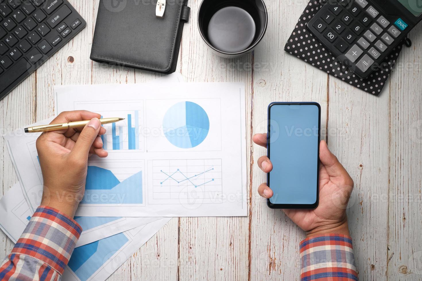 Man hand with pen analyzing bar chart on paper and holding smart phone photo