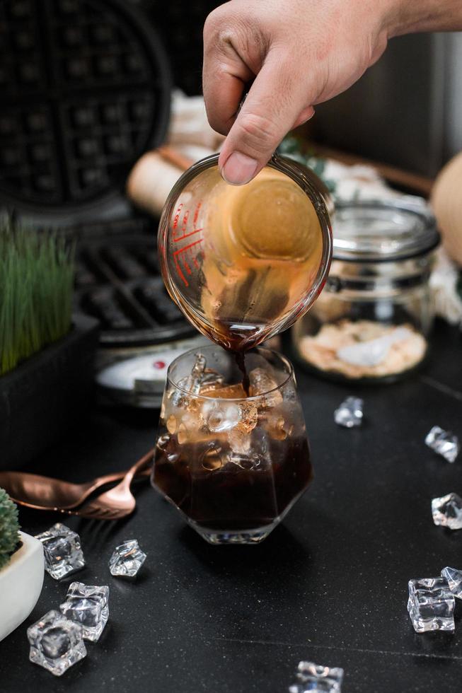 Barista pouring milk into a glass of iced coffee photo