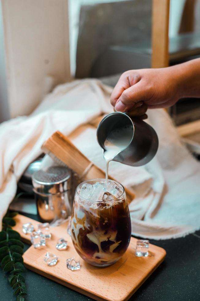 Barista pouring milk into a glass of iced coffee photo