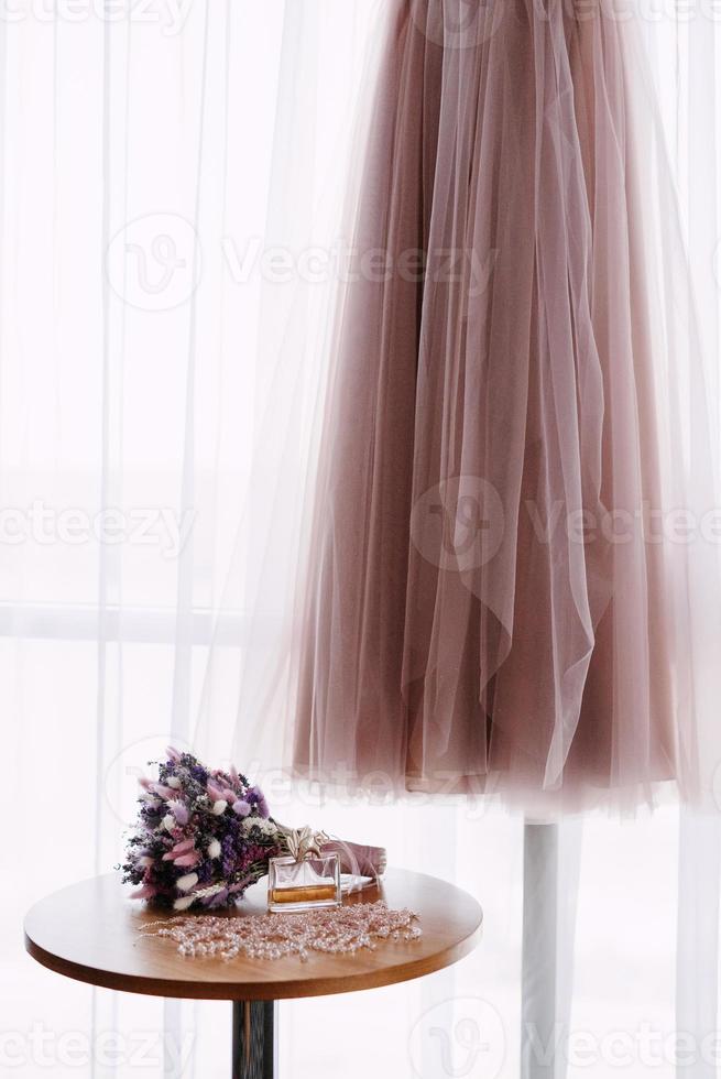 pink wedding dress on the background of the window with the bride's bouquet photo