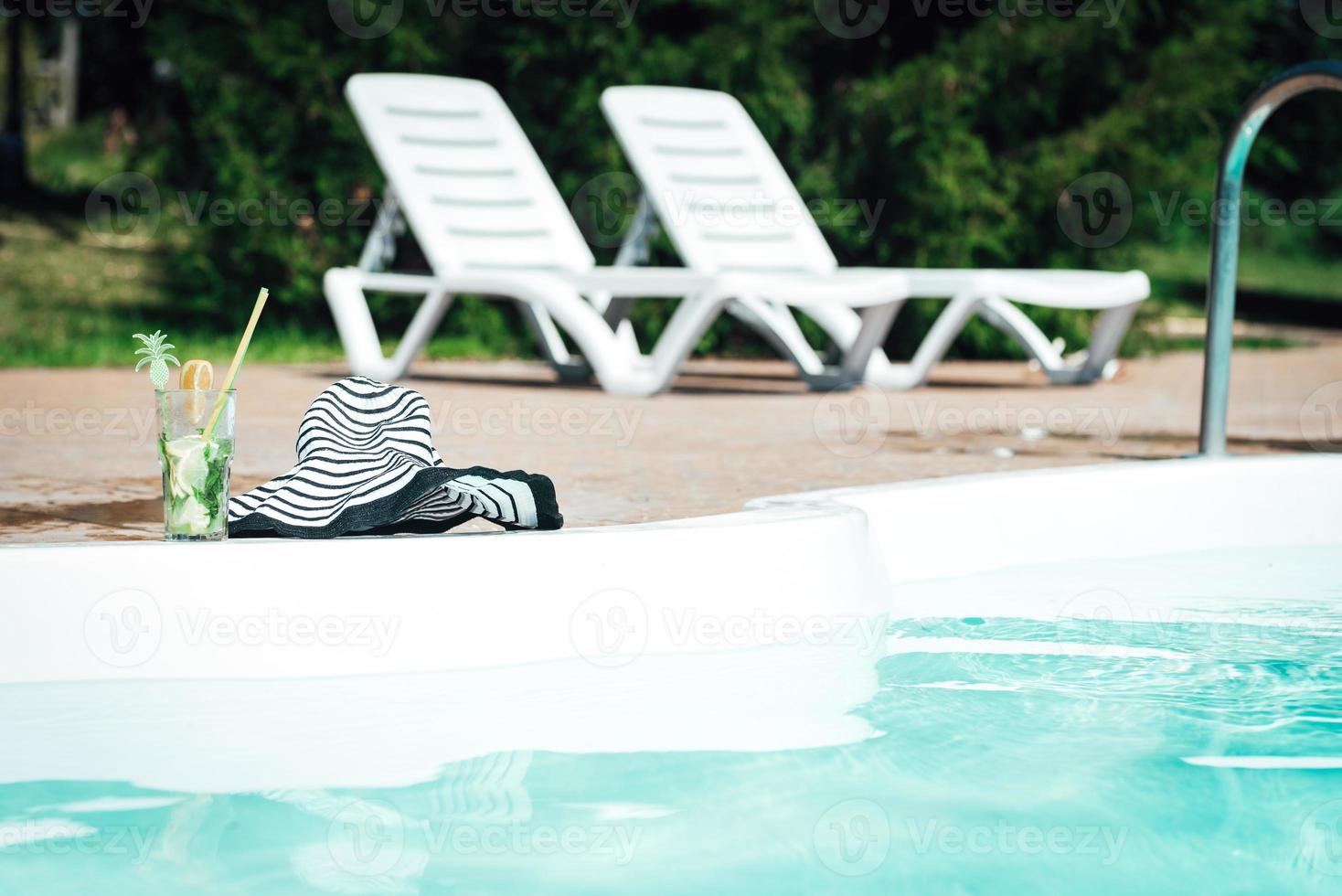 cóctel alcohólico de frutas a base de lima, menta, naranja, refresco de pie en el borde de la piscina foto