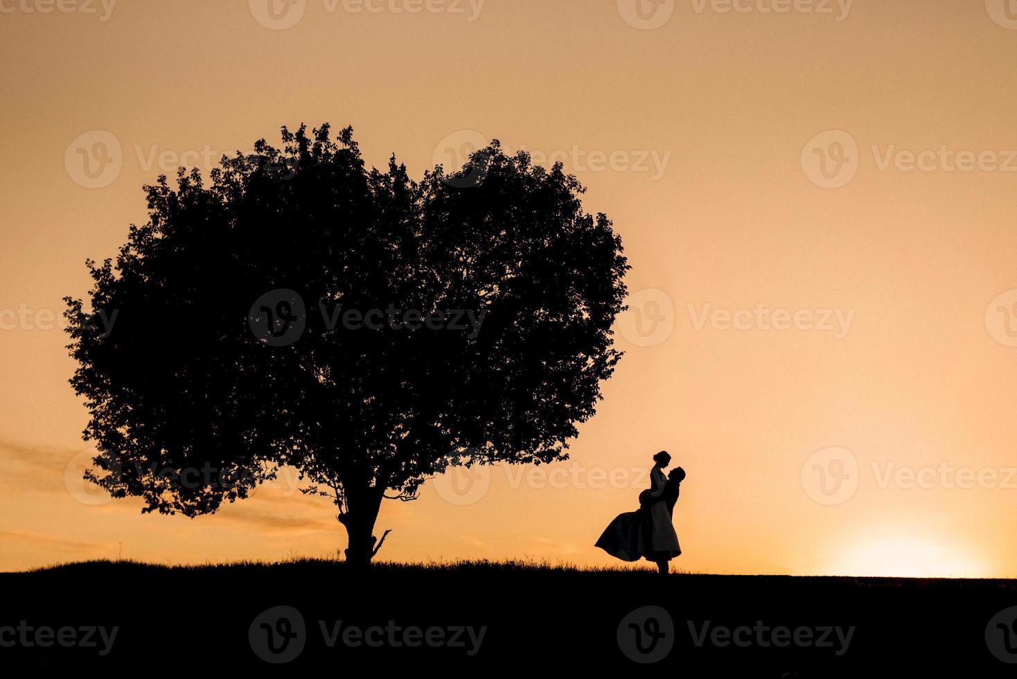 silhouettes of a happy young couple guy and girl on a background of orange sunset photo