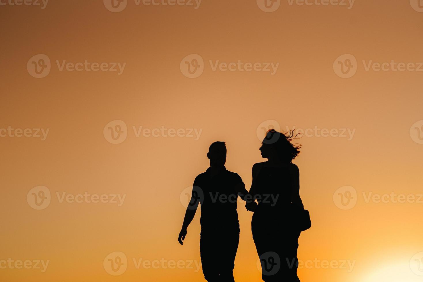 silhouettes of a happy young couple on a background of orange sunset in the sand desert photo