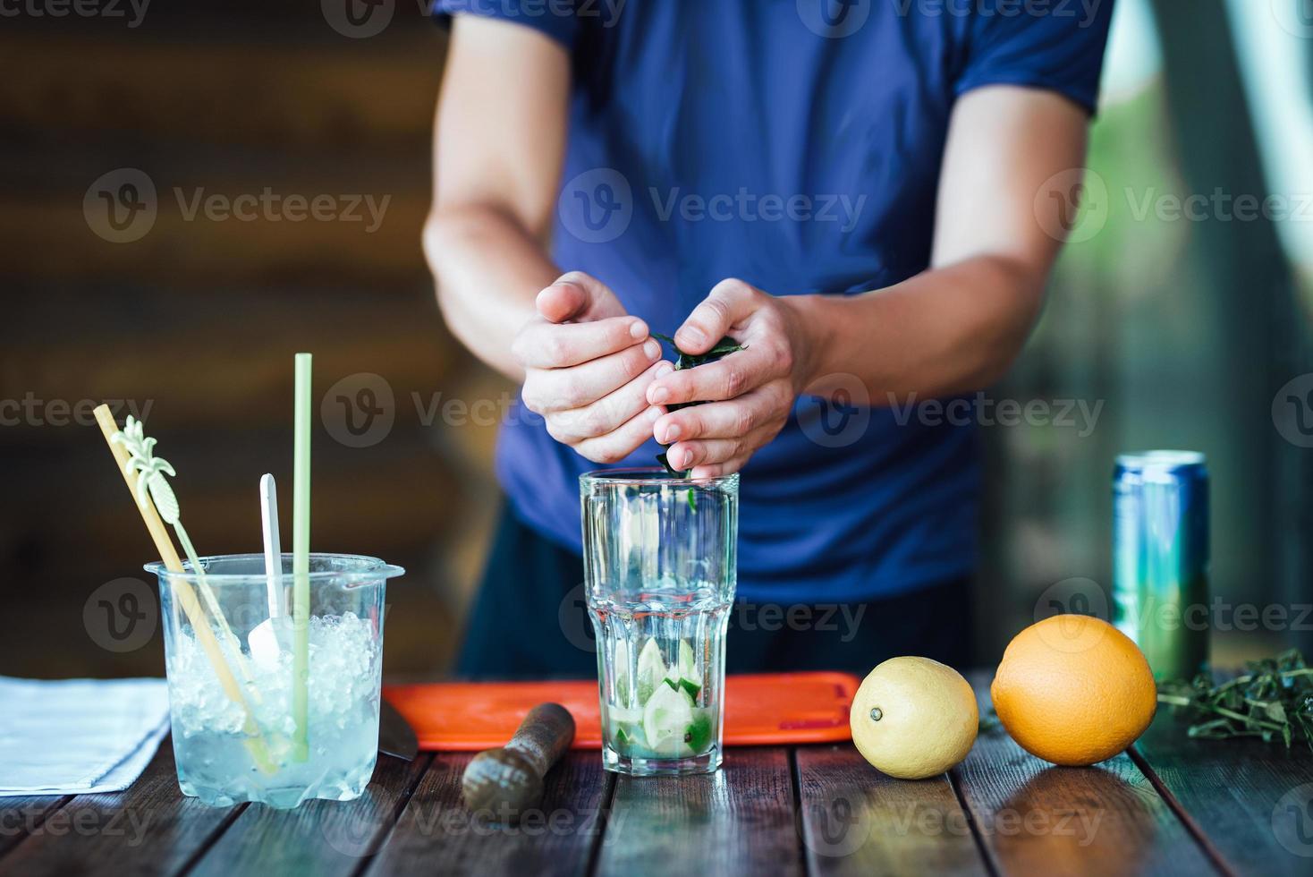 Barman prepares fruit alcohol cocktail based on lime, mint, orange, soda photo