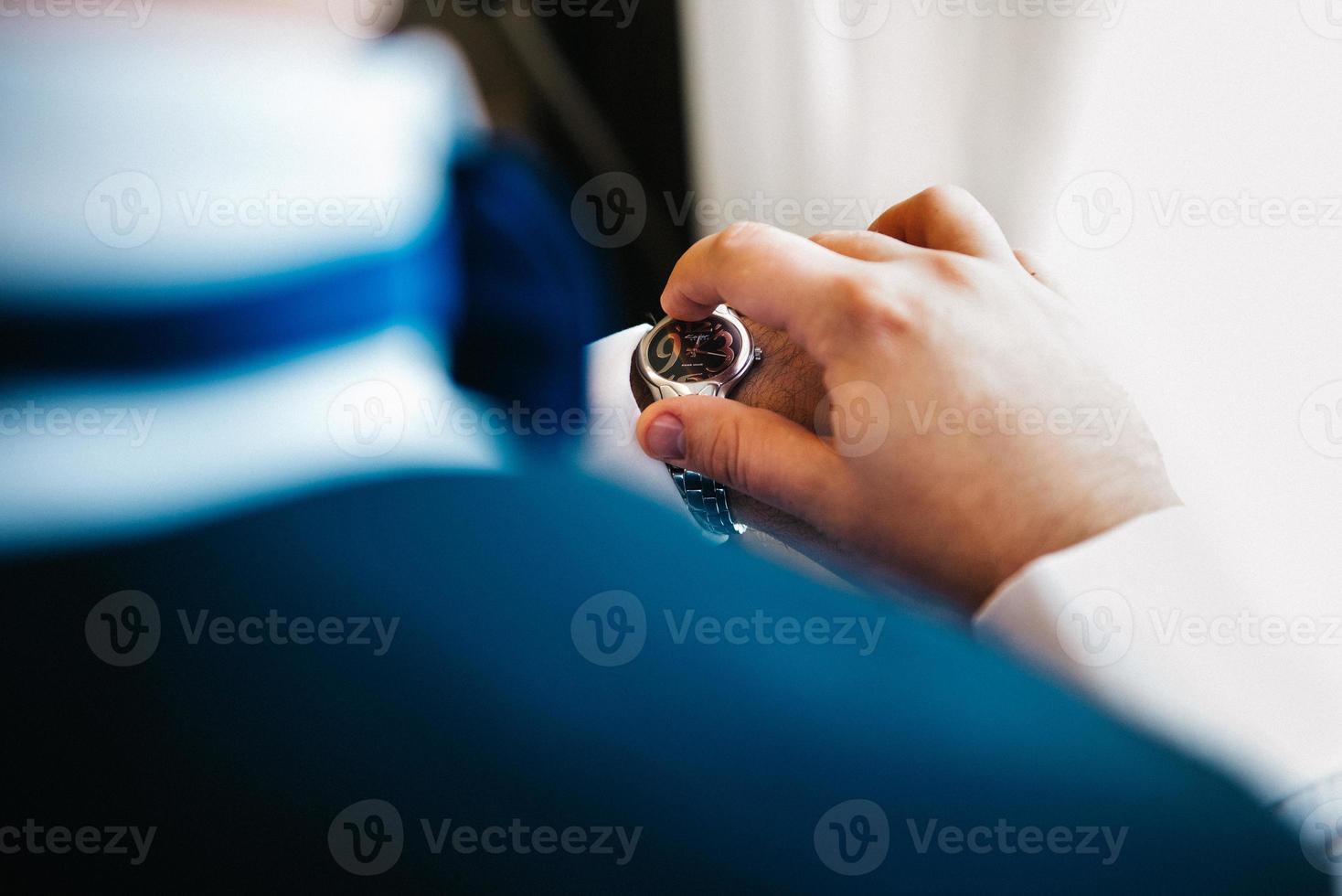 the groom in a blue suit looks at the watch worn on his left hand photo