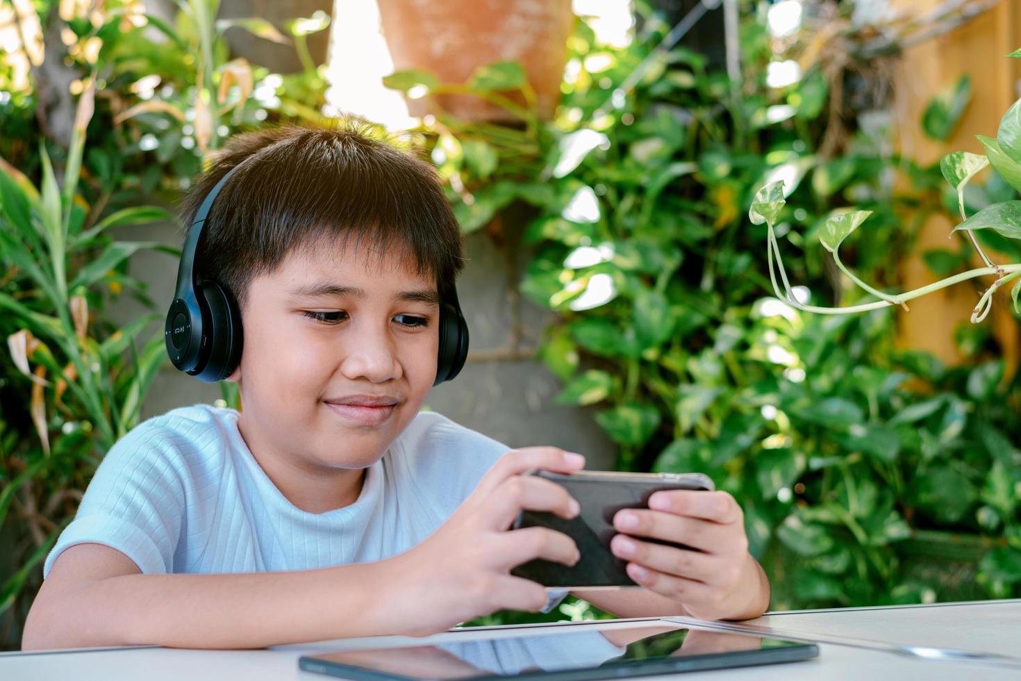 Chico asiático usando audífonos sonriendo y jugando en su teléfono inteligente. foto