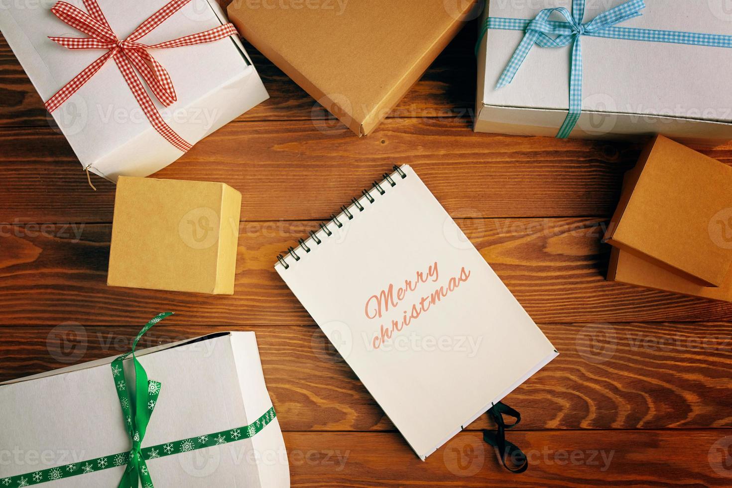 Top view of Merry Christmas notebook and gift boxes on wood table background. photo