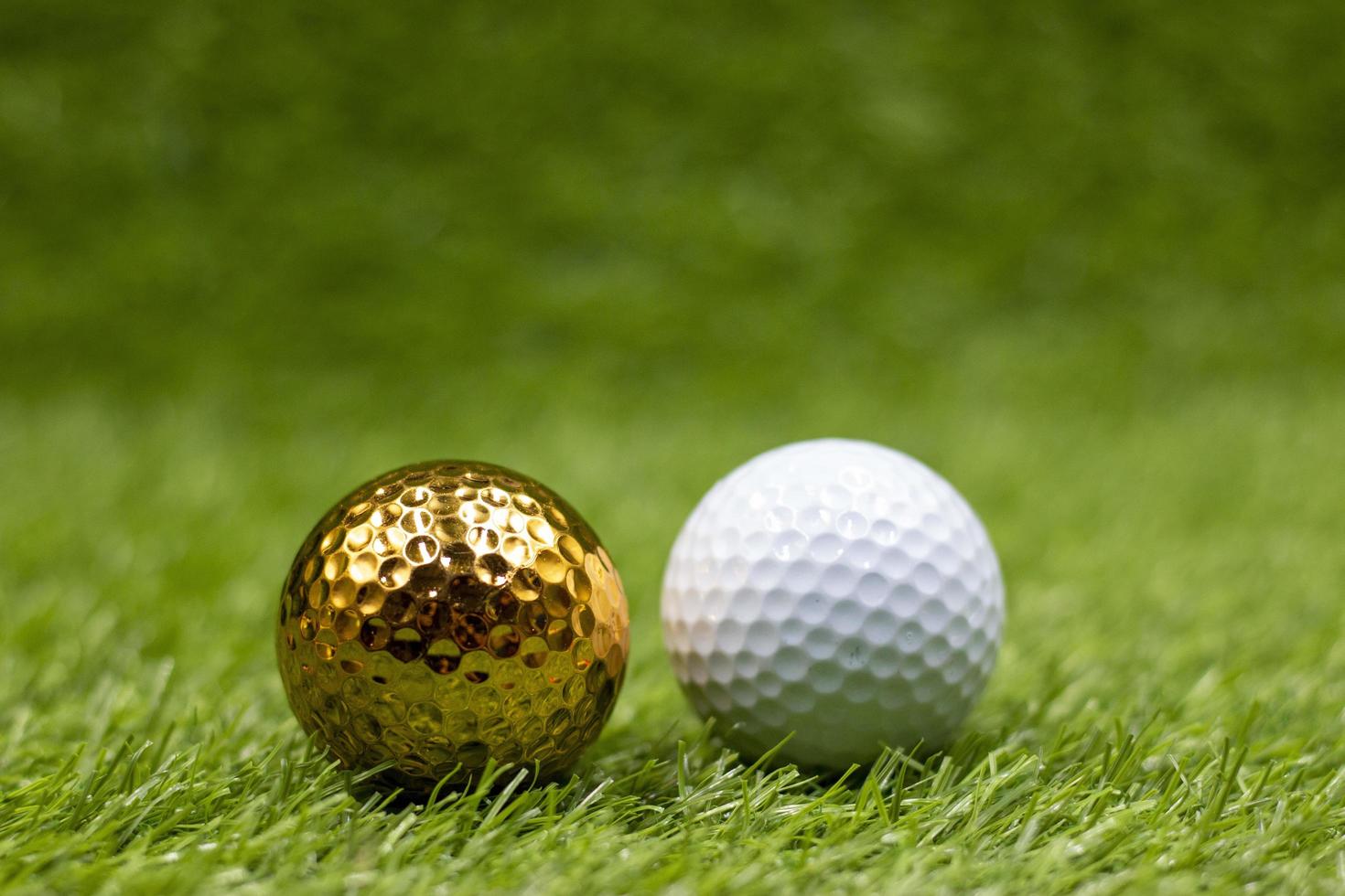 Pelota de golf dorada con pelota de golf blanca sobre la hierba verde foto