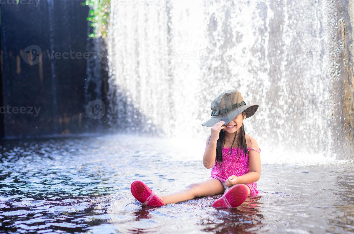 Little Asian girl wear hat playing waterfall on holiday photo