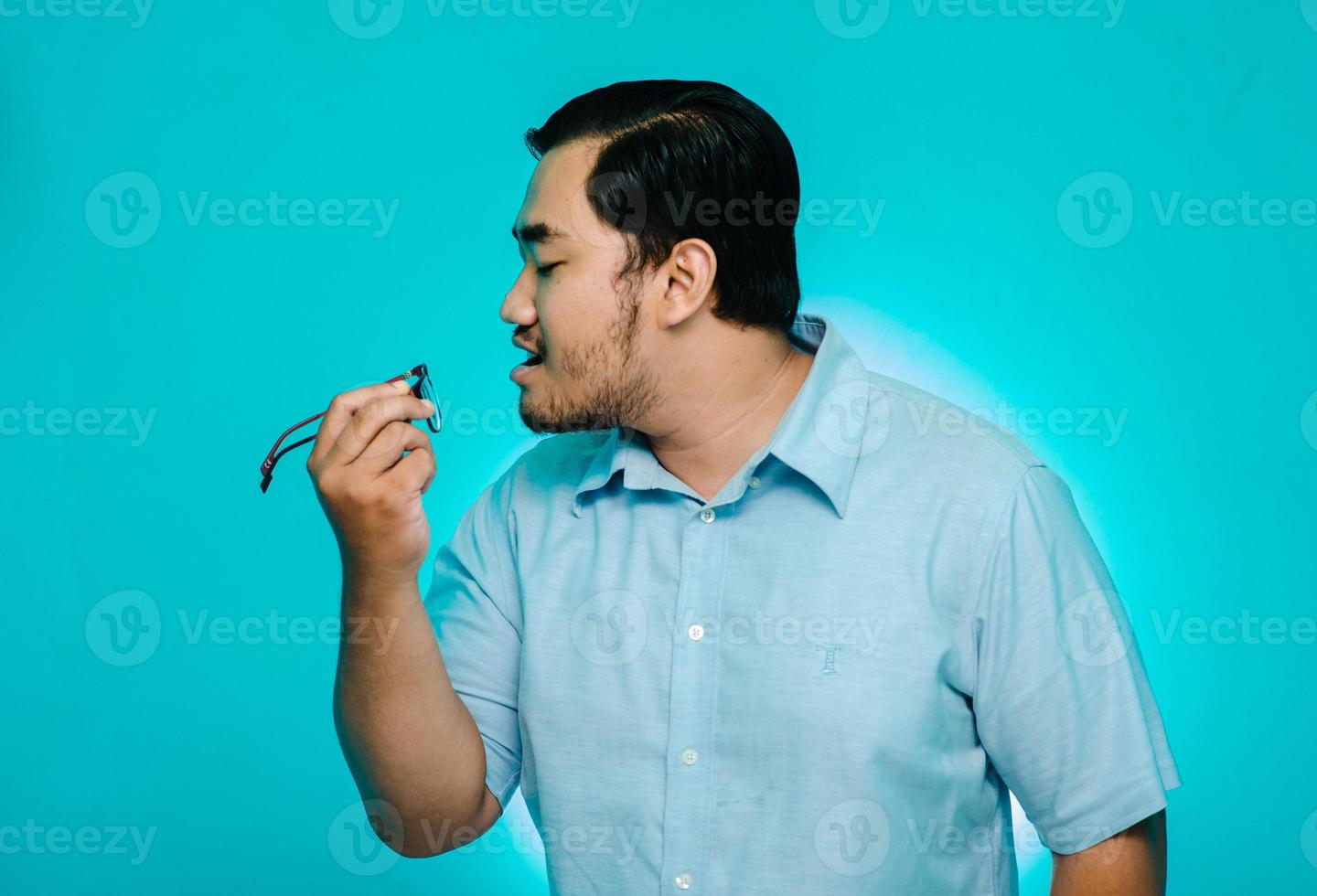 Young man blowing glasses in hand on blue background photo