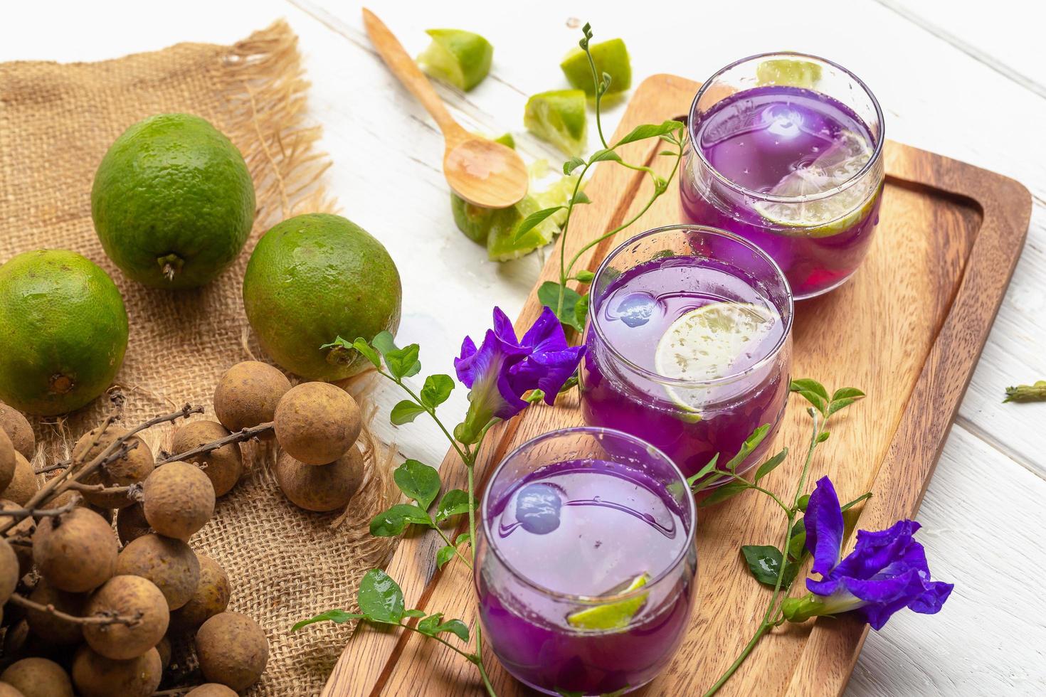 Vaso de jugo de limón, flores de guisantes y longan sobre mesa de madera blanca foto