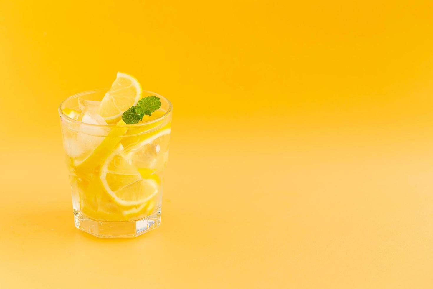 Agua detox con limón en un vaso sobre un fondo naranja foto