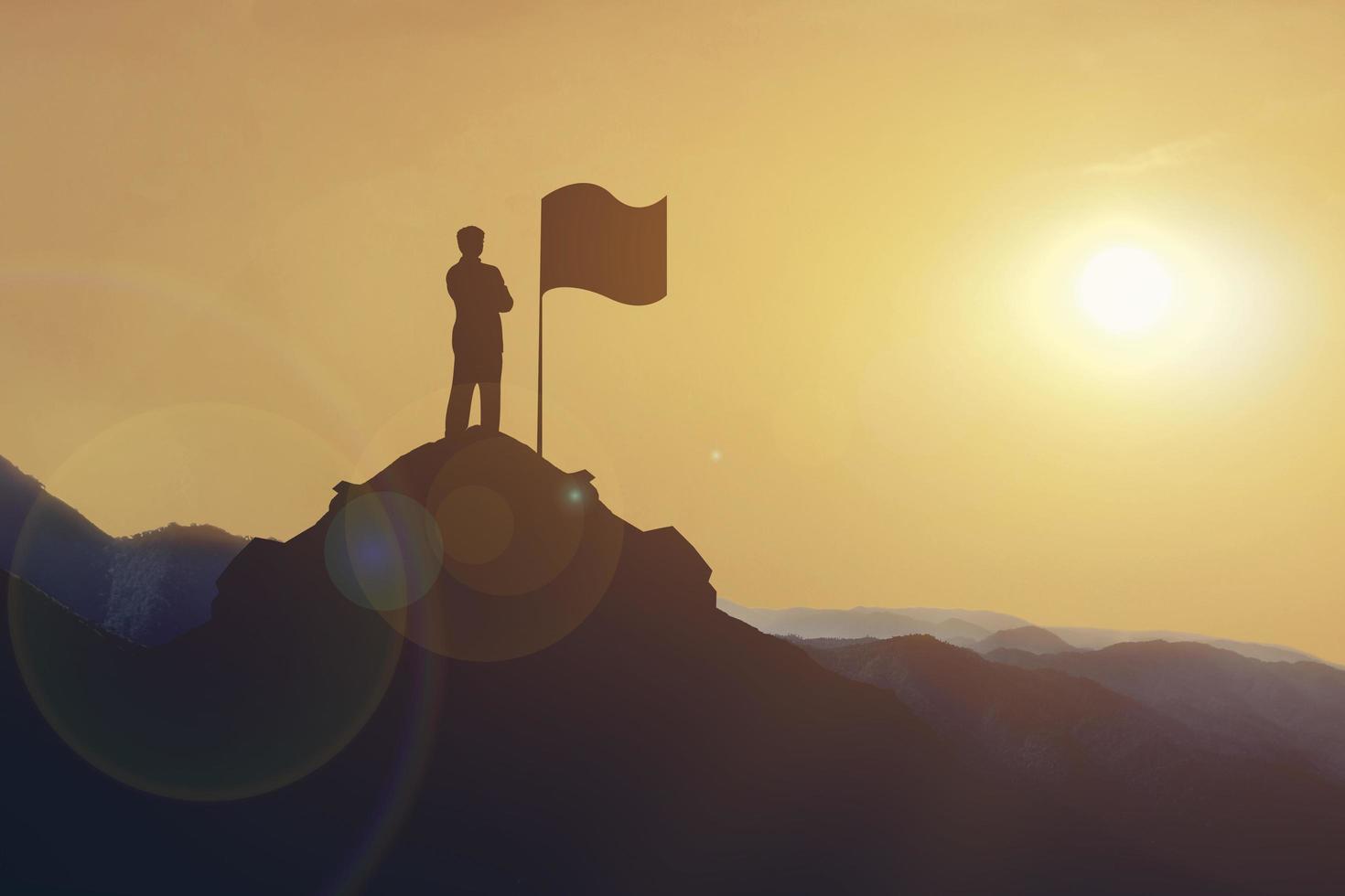 silueta de empresario de pie en la montaña mirando la bandera en la colina al atardecer. objetivo empresarial y concepto de éxito. foto