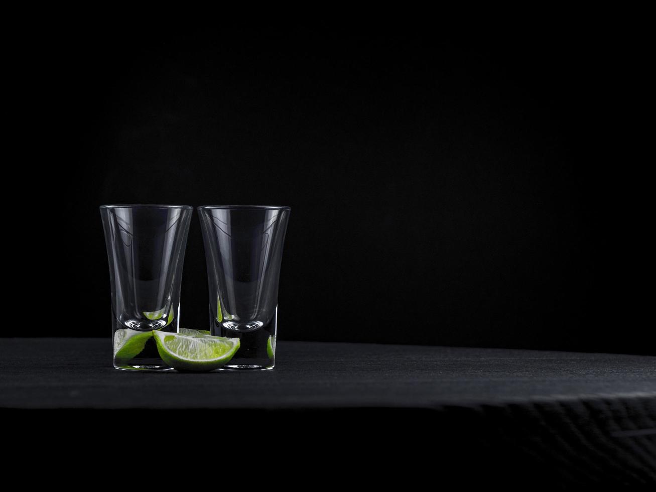 Two empty tequila shots with juicy lime on a dark background photo