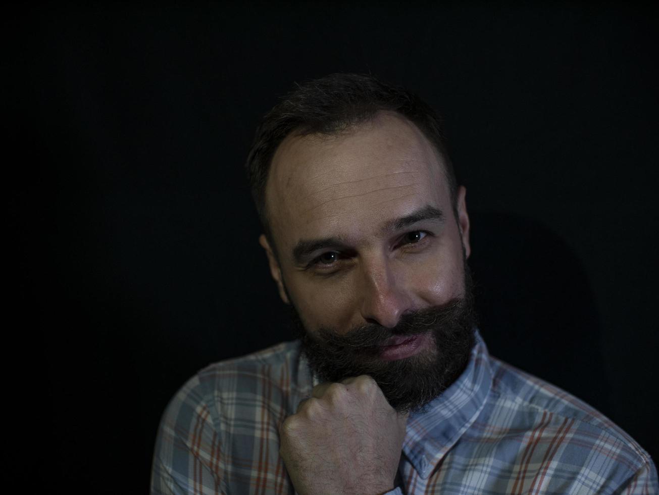 a man with a beard and mustache with a thoughtful sly face on a black background photo