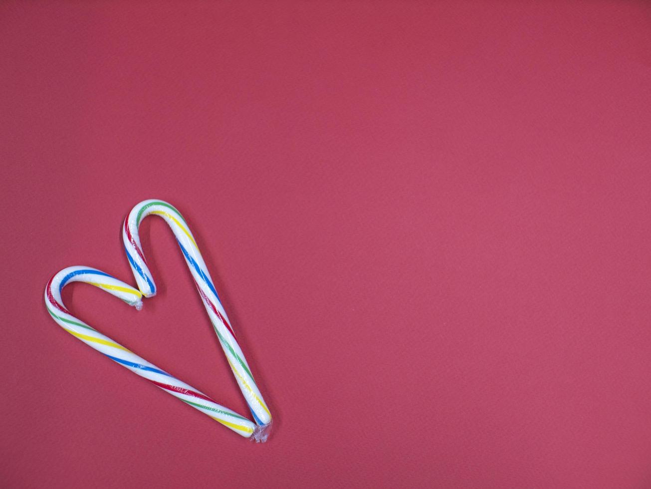 un bastón de caramelo doblado en forma de corazón sobre un fondo rosa foto