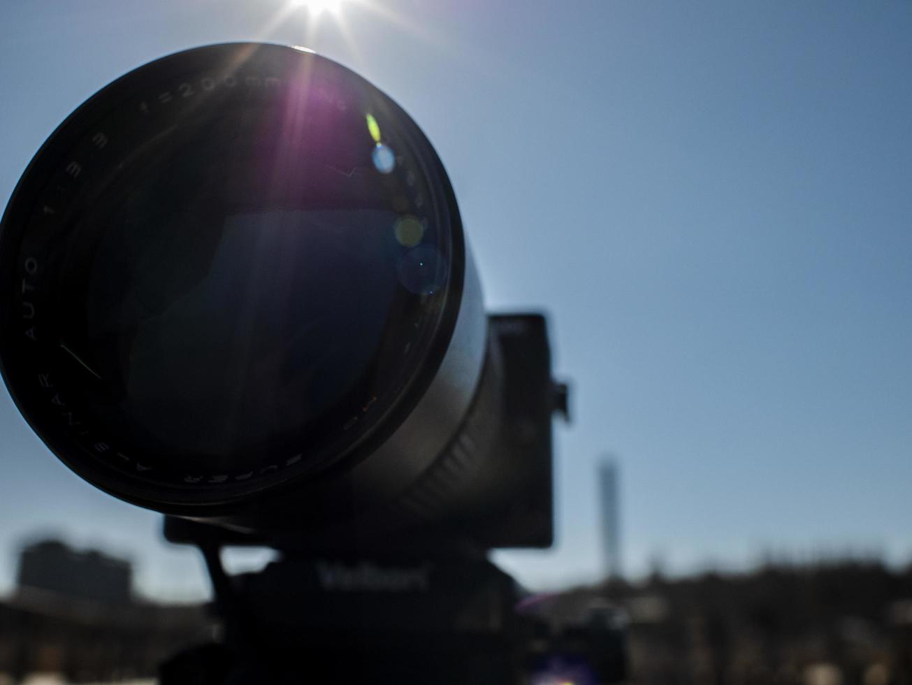 large lens on a tripod in backlight against a blue sky photo
