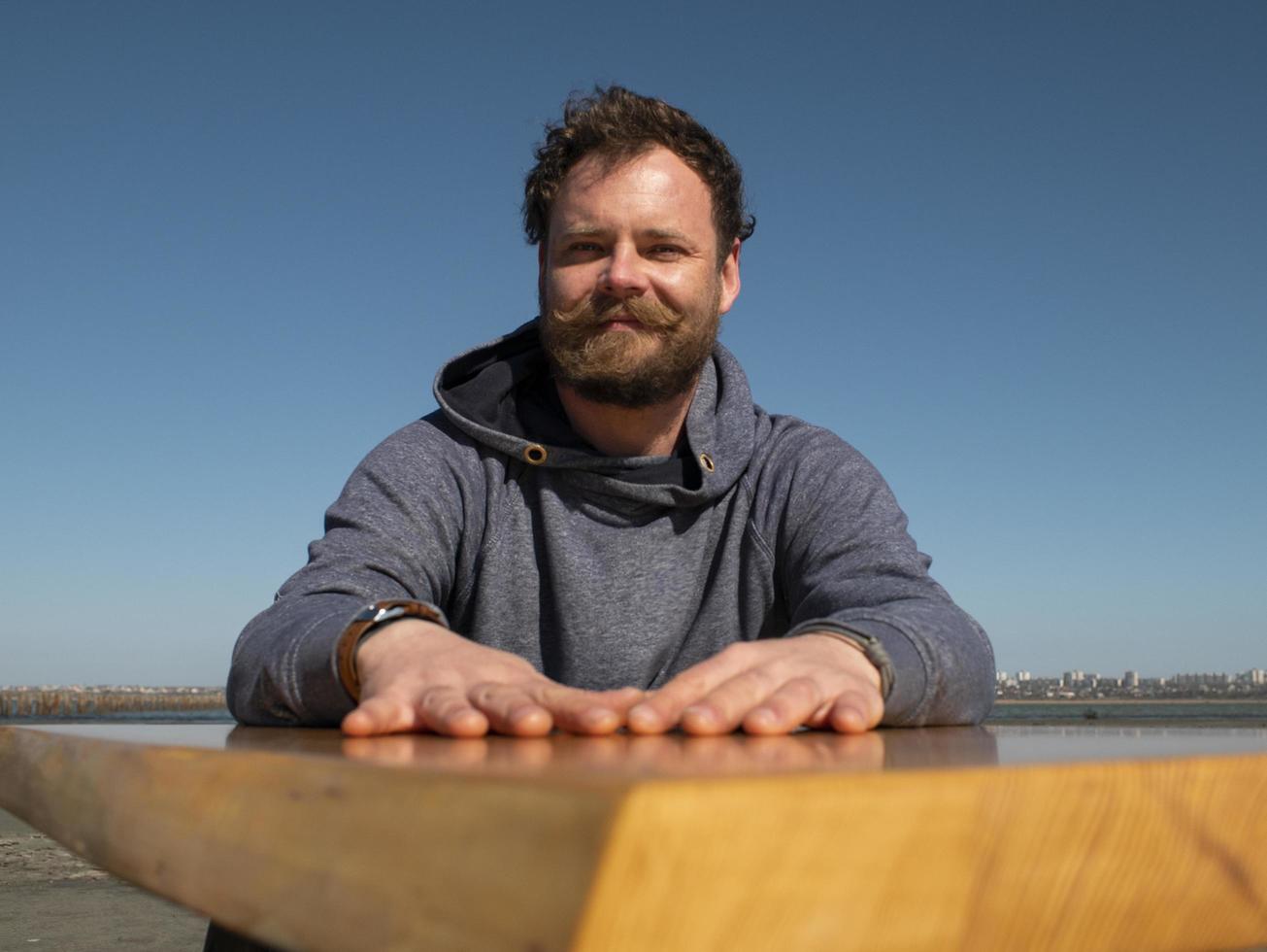 funny man with a beard and mustache sitting at a coffee table against a blue sky photo