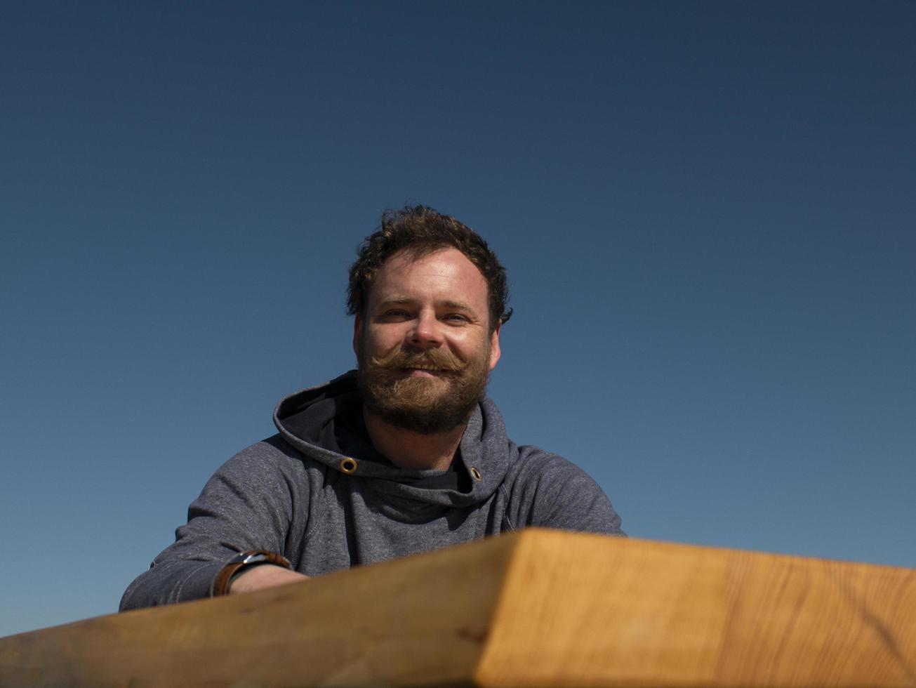 funny man with a beard and mustache sitting at a coffee table against a blue sky photo