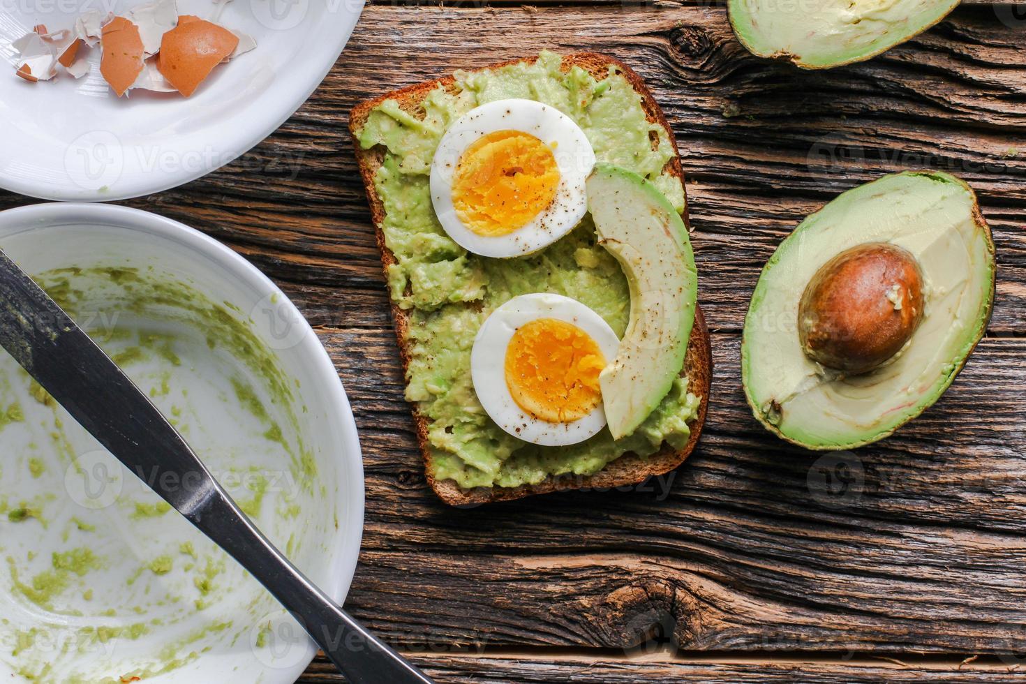 Tostadas con puré de aguacate y huevos en la desordenada mesa de madera rústica foto