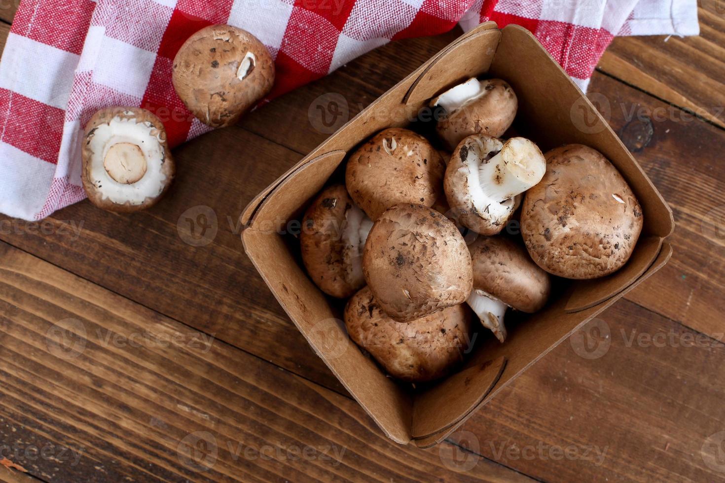 Baby bella mushrooms inside paper container on wooden table with cotton napkin photo