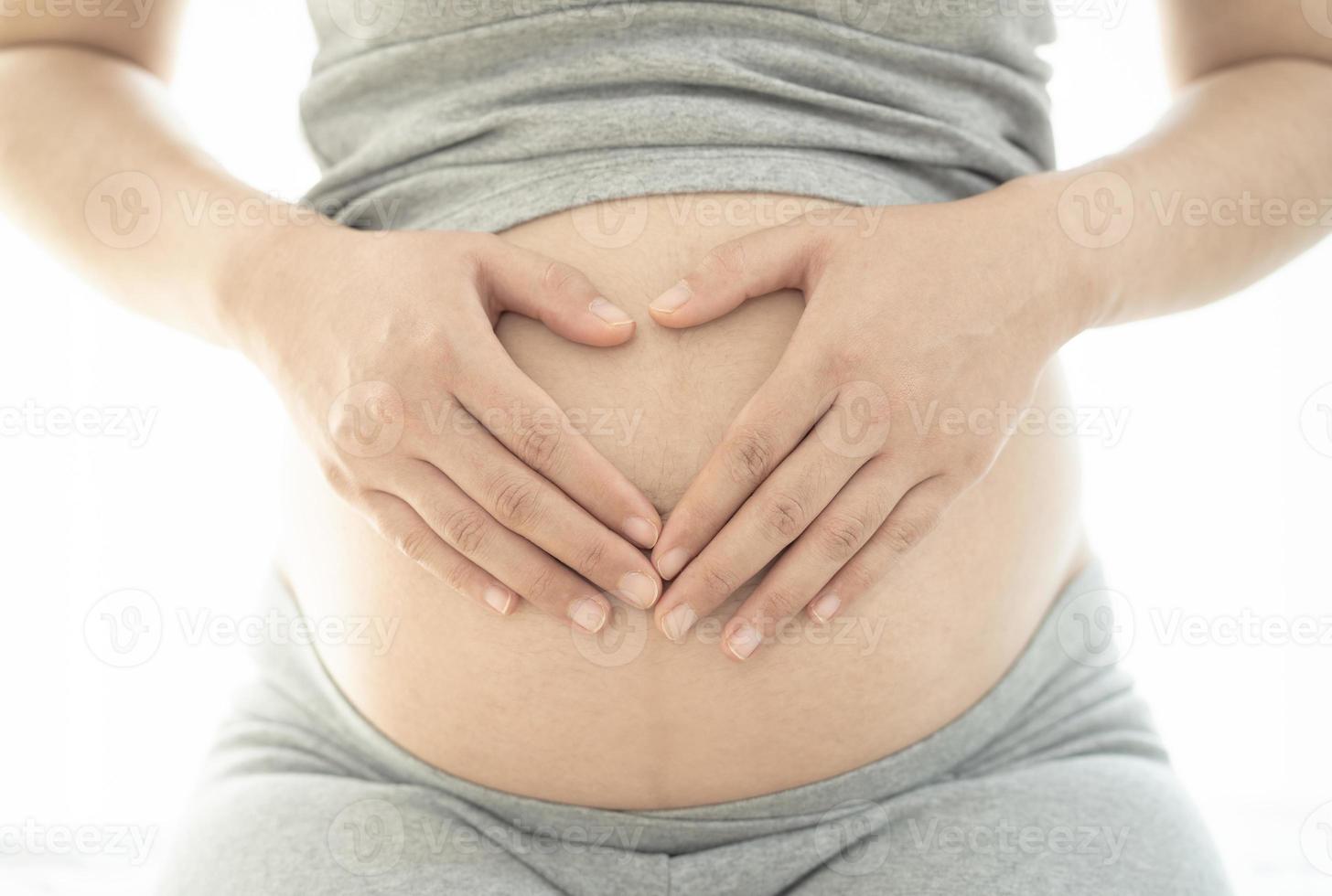 Close up of pregnant woman making heart shape hand sign on her bare tummy photo