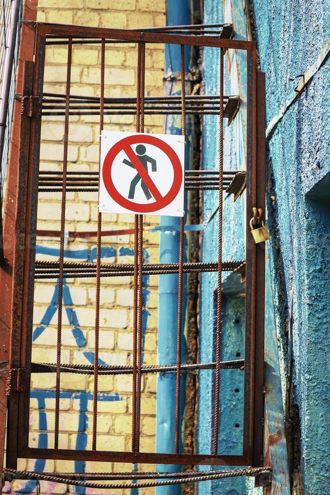 No walking sign on rusty iron fence foor near blue textured wall photo