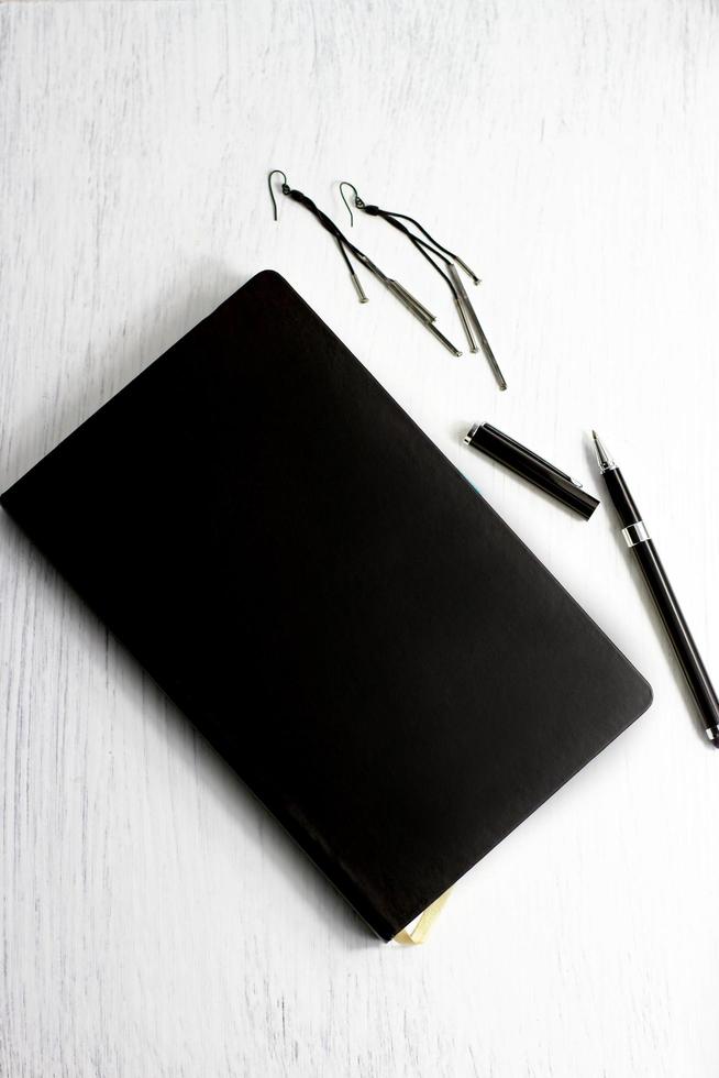 Earrings black leather notebook and pen on white wooden table, business set and jewelry photo