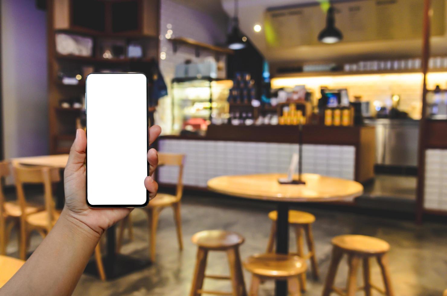 Hand holding phone mockup image blank screen for advertising text in vintage cafe coffee shop background photo