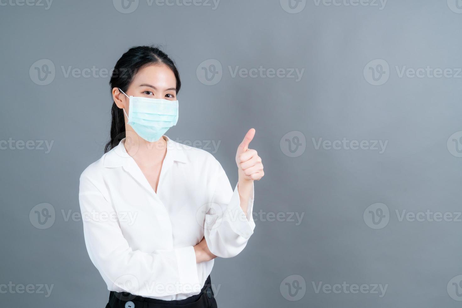 Joven mujer asiática con mascarilla médica y dando pulgares hacia arriba foto