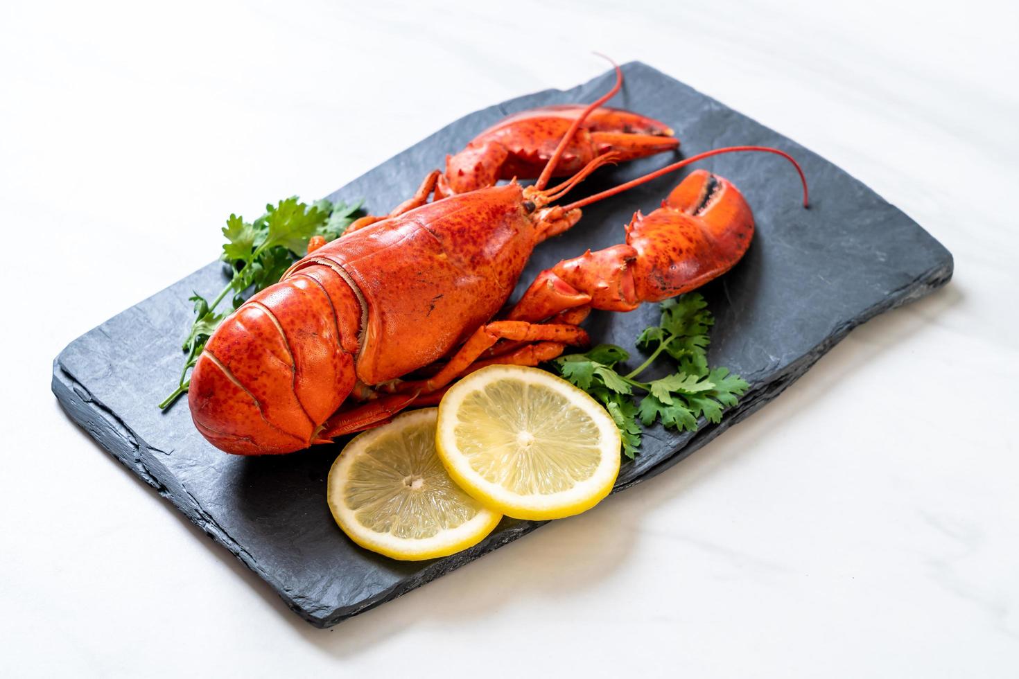 Langosta roja con verduras y limón sobre placa de pizarra negra foto