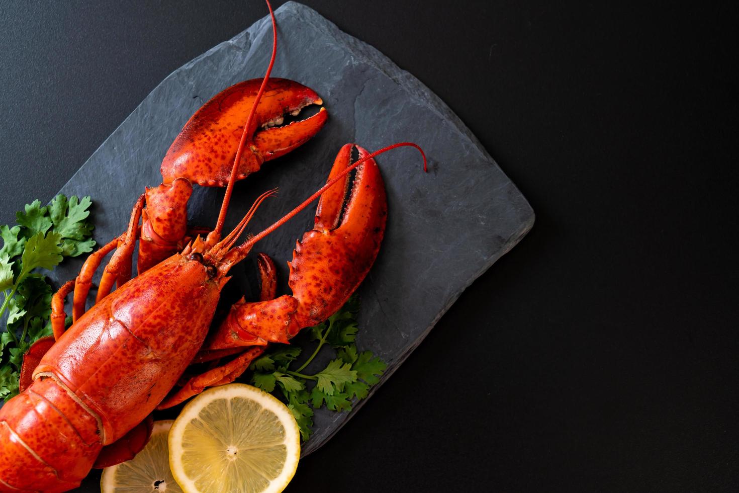 Langosta roja con verduras y limón sobre placa de pizarra negra foto