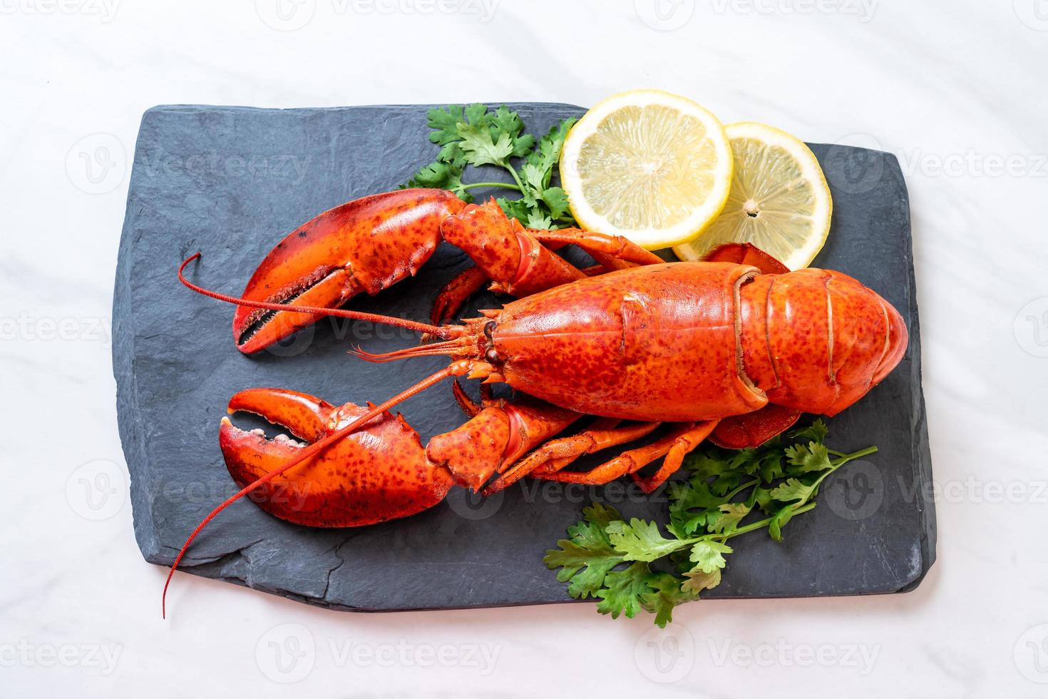 Langosta roja con verduras y limón sobre placa de pizarra negra foto