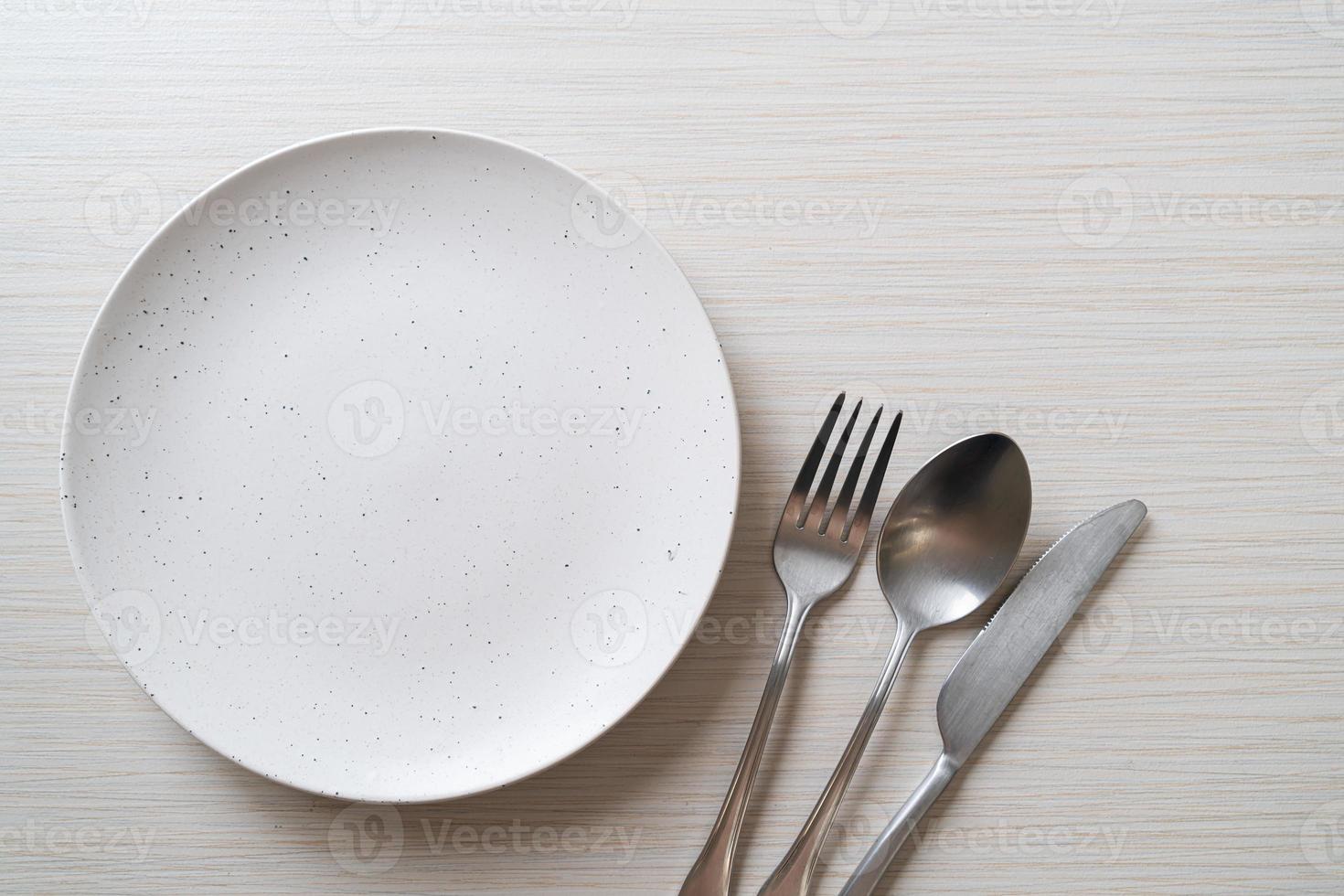 Empty plate or dish with knife, fork, and spoon on wood tile background photo