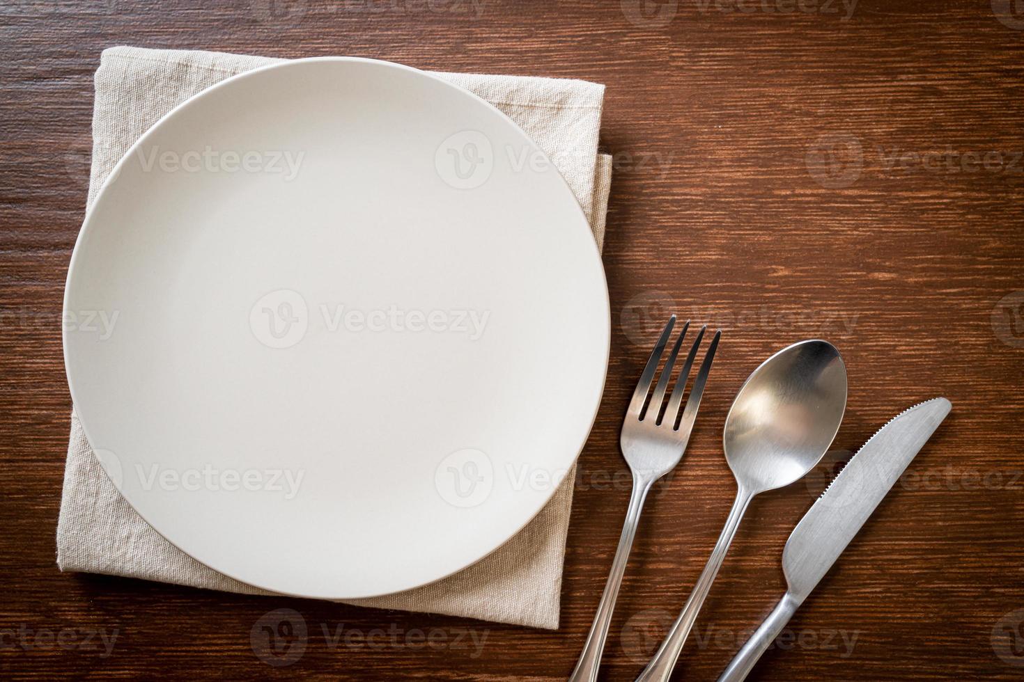 Empty plate or dish with knife, fork, and spoon on wood tile background photo