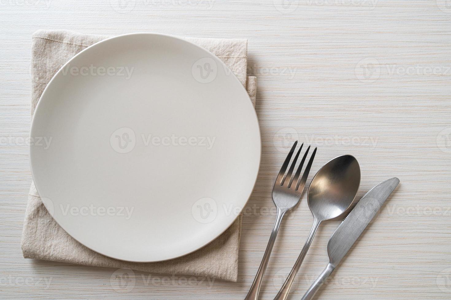 Empty plate or dish with knife, fork, and spoon on wood tile background photo