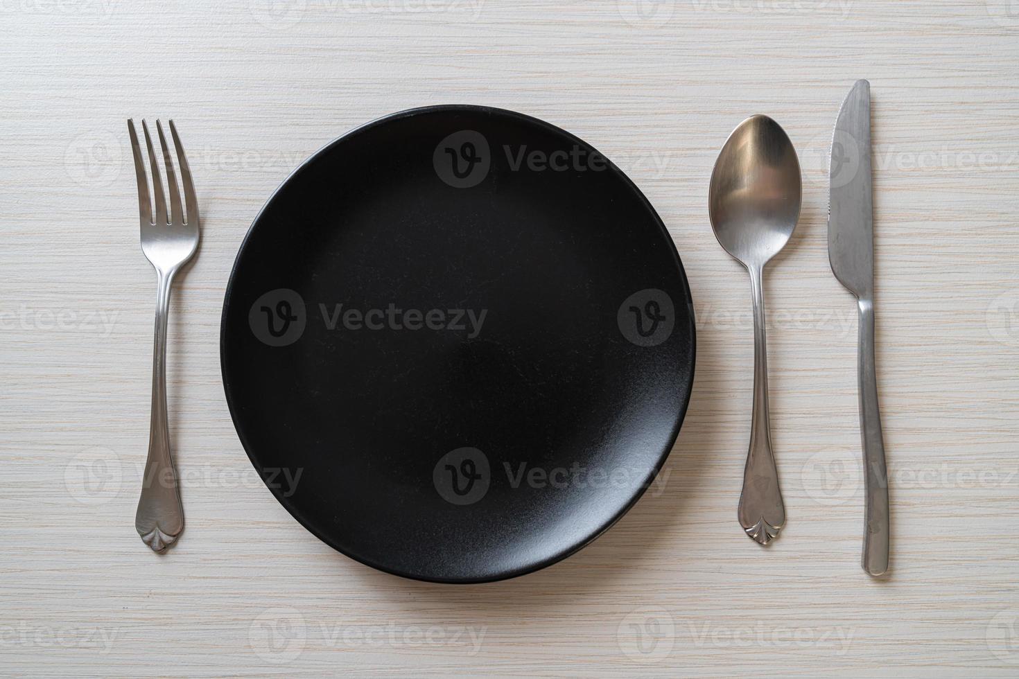 Empty plate or dish with knife, fork, and spoon on wood tile background photo